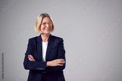 Studio Portrait Of Smiling Mature Businesswoman Wearing Glasses Against Plain Background