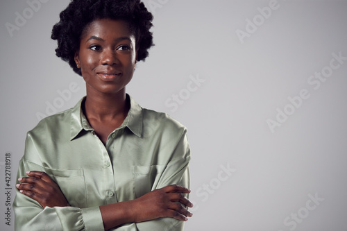 Close Up Studio Portrait Of Smiling Young Businesswoman With Folded Arms Against Plain Background