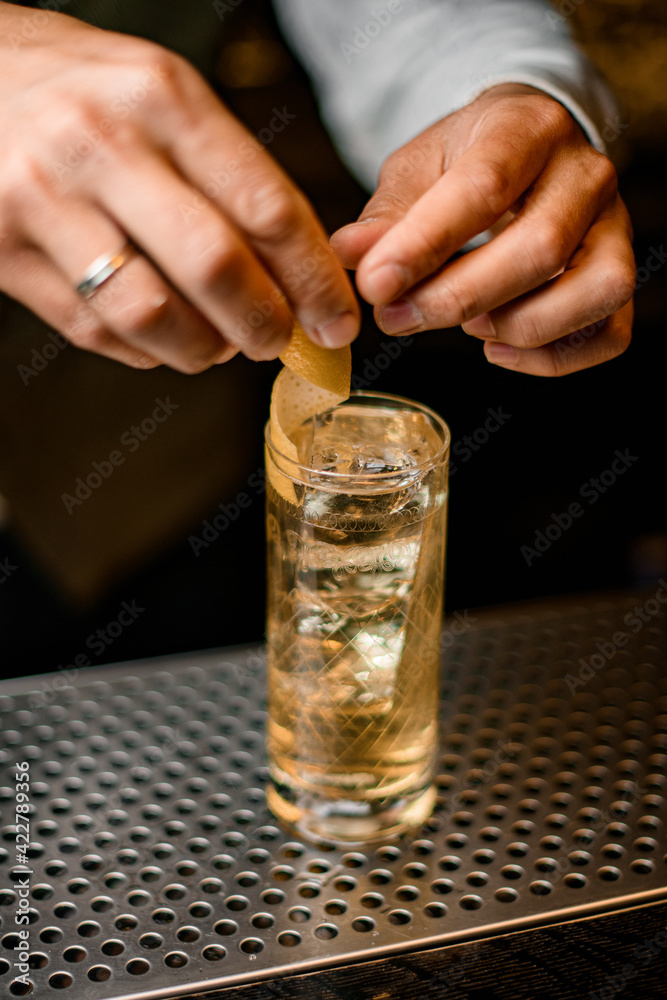 close-up of crystal glass with cold drink which barman's hands decorate with orange peel