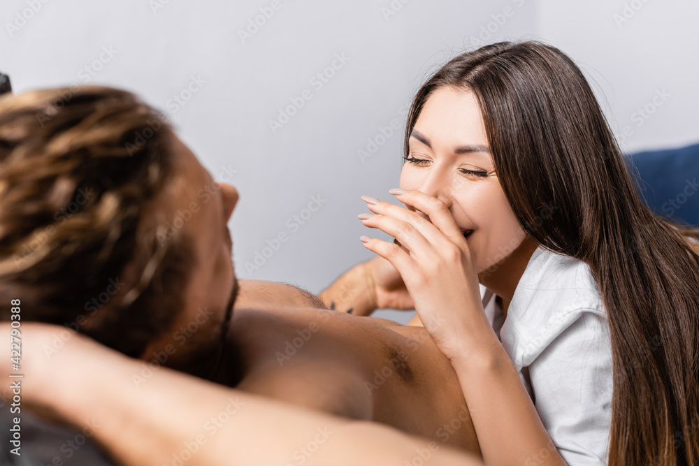 Cheerful woman smiling near shirtless boyfriend on blurred foreground at home Cheerful woman smiling near shirtless boyfriend on blurred foreground at home