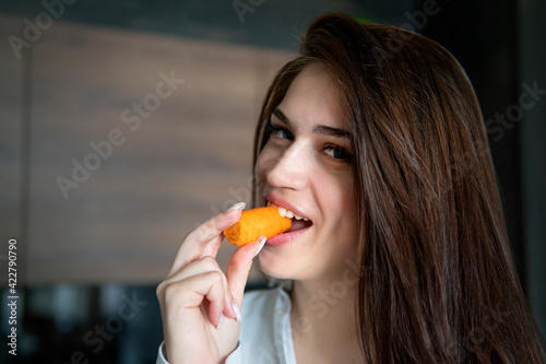 Close up woman eating nibbling carrot and smiling in the kitchen interior.. Health diet food. nibble on a carrot