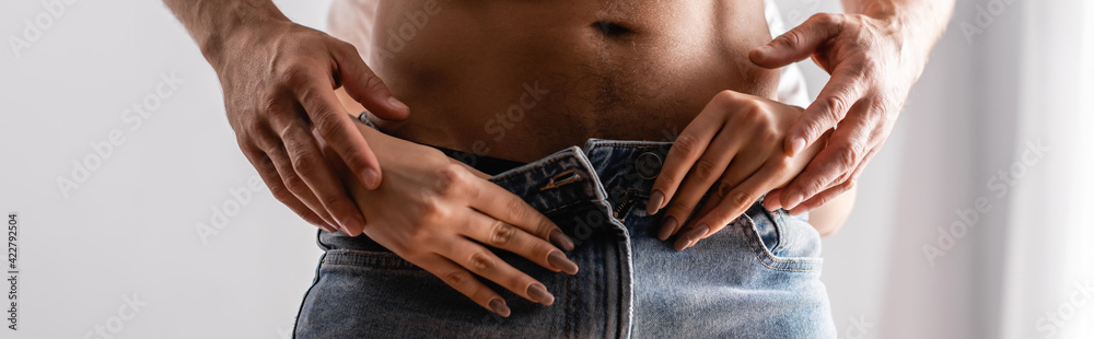 Cropped view of passionate woman taking off jeans from boyfriend, banner