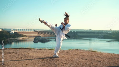 young woman white kimono demonstrates karate technique against backdrop nature