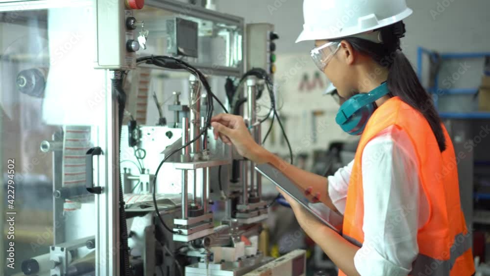 Asian woman who is an industrial engineer working on machines and working at an industrial machine with a digital tablet. heavy work Concept of industrial workers Asian woman who is an industrial engineer working on machines and working at an industrial machine with a digital tablet. heavy work Concept of industrial workers