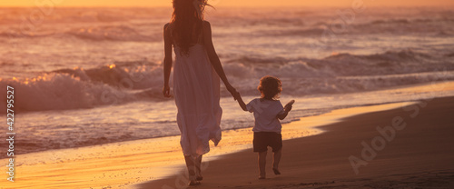 Fotografie A mom with her child walk on the beach of a beautiful shore at the sunset light