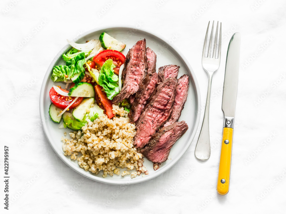 Balanced lunch - medium roast steak, vegetable salad and bulgur on a light background, top view Balanced lunch - medium roast steak, vegetable salad and bulgur on a light background, top view