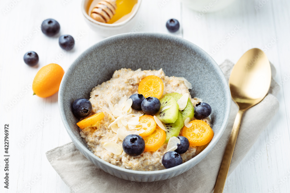 Oatmeal porridge with kumquat, blueberries, kiwi and almond flakes in a bowl. Healthy breakfast on a white table.