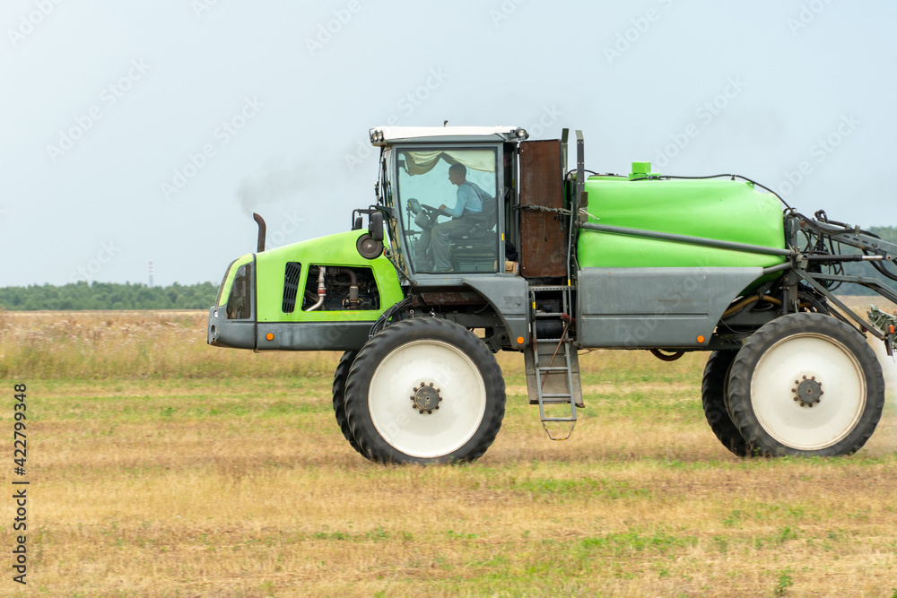 Fototapeta premium self-propelled sprayer works on a field on a warm sunny day. Spraying the Crop. Tractor with the help of a sprayer sprays liquid fertilizers in the field.