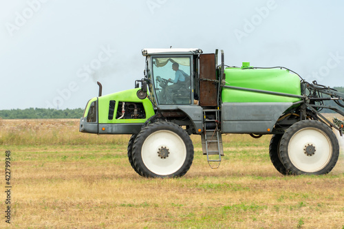 self-propelled sprayer works on a field on a warm sunny day. Spraying the Crop. Tractor with the help of a sprayer sprays liquid fertilizers in the field.