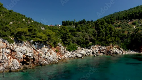 Aerial drone views over a rocky coastline, crystal clear Aegean sea waters, touristic beaches and lots of greenery in Skopelos island, Greece. A typical view of many similar Greek islands.