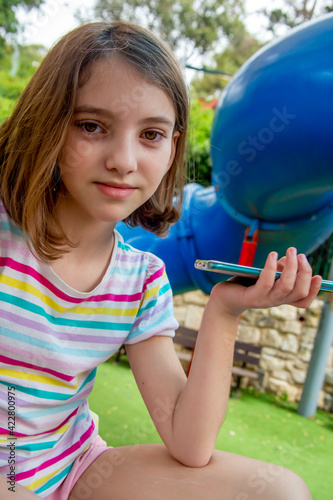 cute happy beautiful natural teenage girl in striped light t-shirt and pink shorts with mobile telephone on the playground