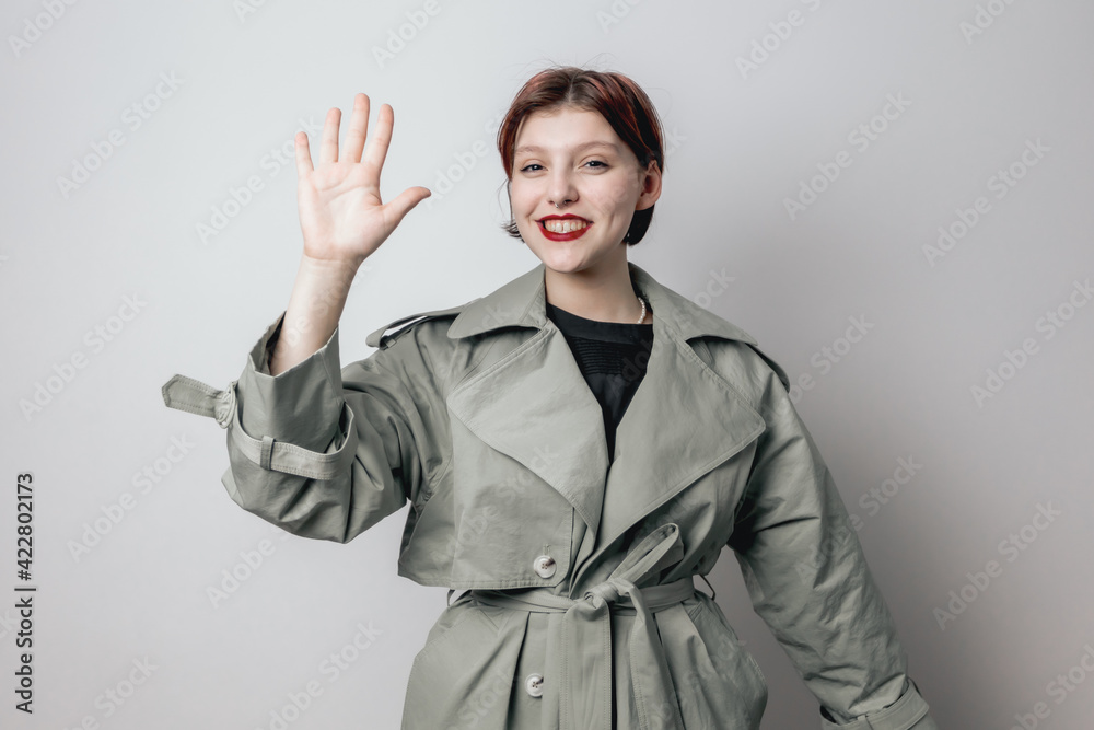 Smiling girl in a fashionable green coat shows the palm of her hand. White background Smiling girl in a fashionable green coat shows the palm of her hand. White background
