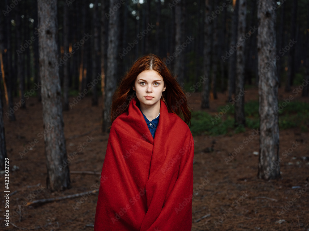 A red-haired woman with a plaid on her shoulders walks in the forest near the trees A red-haired woman with a plaid on her shoulders walks in the forest near the trees