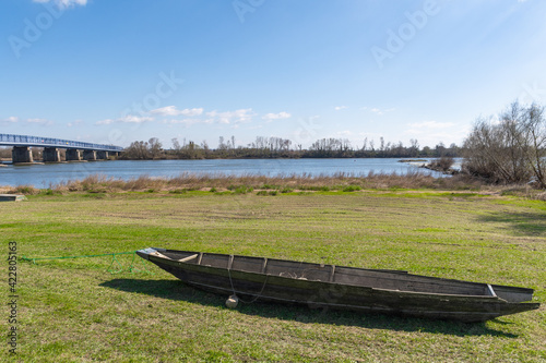 wooden boat on grass with river abd steel bridge in background