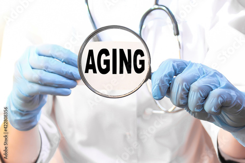 the doctor in gloves holds a magnifying glass with the text AGING . the medicine