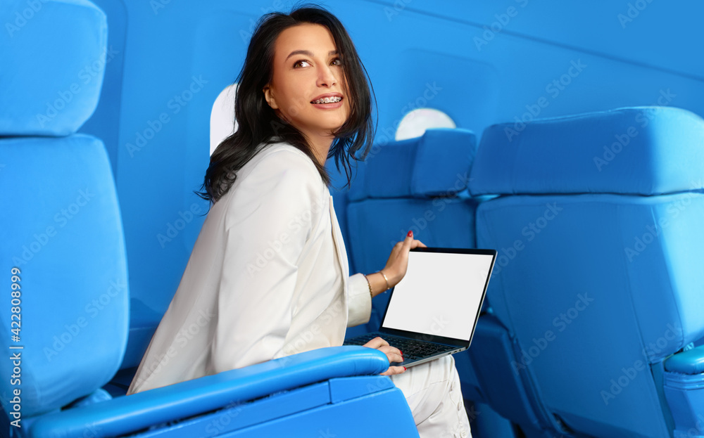 Businesswoman in a white suit using laptop sitting at the first class on the airplane during flight. Female working on a laptop with Wi-Fi internet access onboard in the airplane blue's cabin. Businesswoman in a white suit using laptop sitting at the first class on the airplane during flight. Female working on a laptop with Wi-Fi internet access onboard in the airplane blue's cabin.