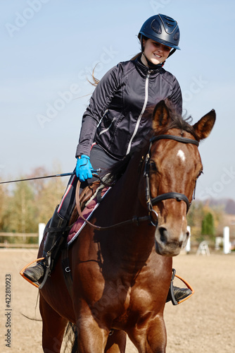 Young horsewoman riding on brown horse in paddok outdoors, copy space. Equestrian sport. © mirage_studio