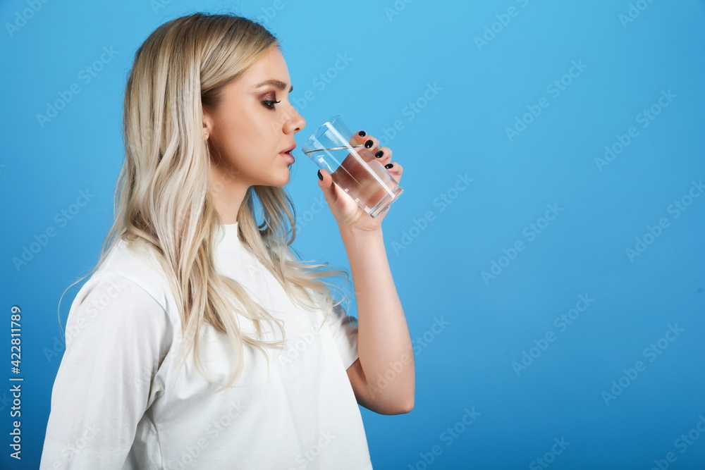 young woman drinking water on blue background. girl holding a glass of water young woman drinking water on blue background. girl holding a glass of water