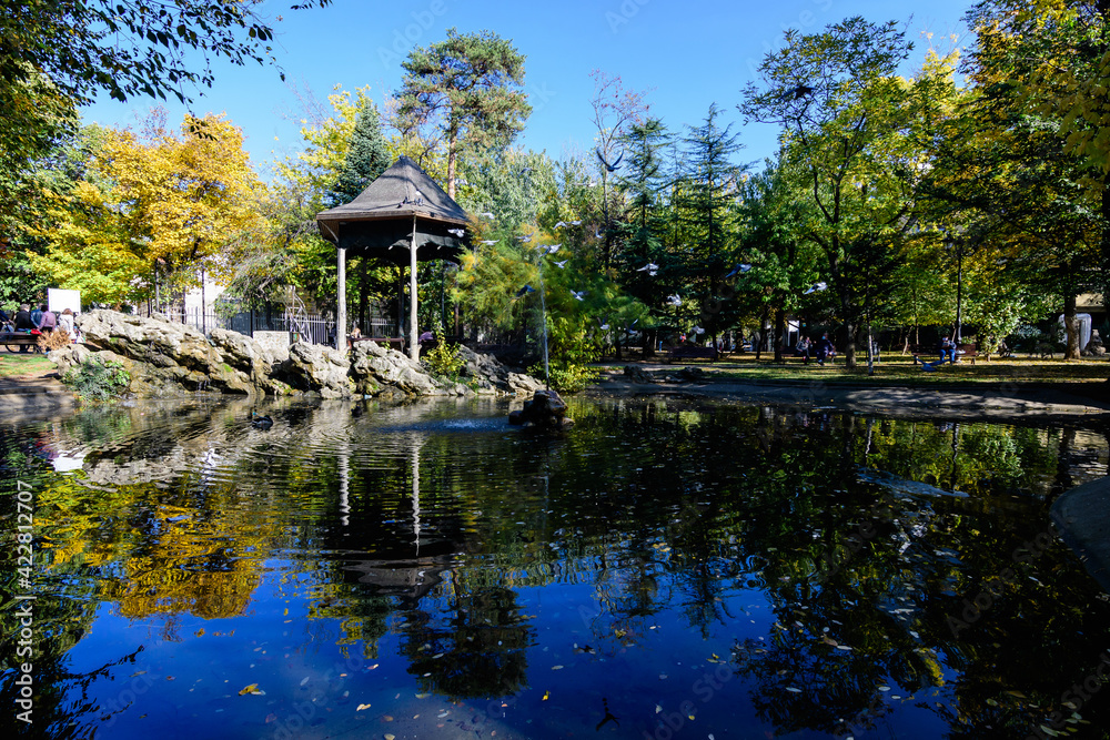 Landscape with the small lake and green and yellow trees in Ion Voicu Park, also known as Ioanid Park, in Bucharest, Romania, in a sunny autumn day. Landscape with the small lake and green and yellow trees in Ion Voicu Park, also known as Ioanid Park, in Bucharest, Romania, in a sunny autumn day.