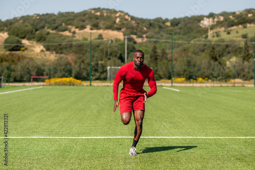 Professional black afro runner training in a field.