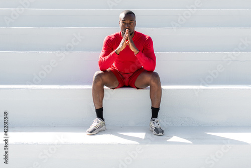 Photography African sportsman with red sportswear sitting on white stairways in a stadium