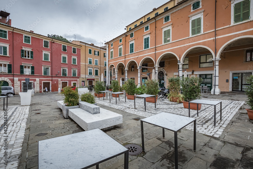 Cityscape. Carrara city center: Piazza Alberica with the commemorative monument in the center and the Ducal Palace , and small open doors cafes, shops in Tuscany, Italy