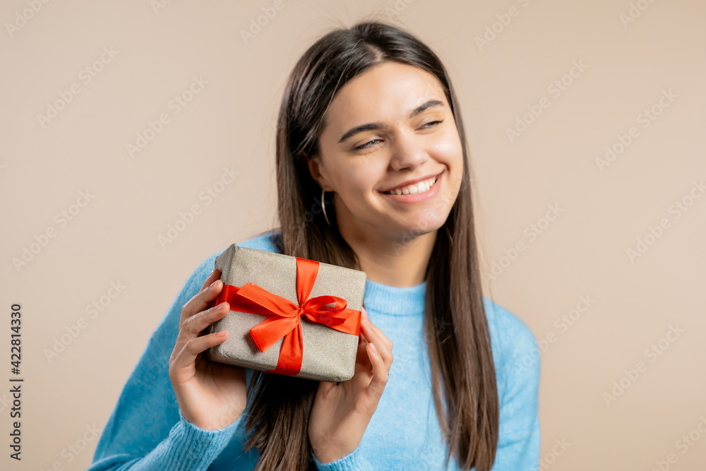 Excited woman received gift box with bow. She is happy and flattered by attention. Girl smiling with present on light background. Studio portrait Excited woman received gift box with bow. She is happy and flattered by attention. Girl smiling with present on light background. Studio portrait