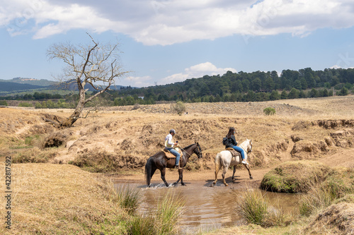 Dos jóvenes con sus caballos están cruzando un arroyo. © jesuschurion57