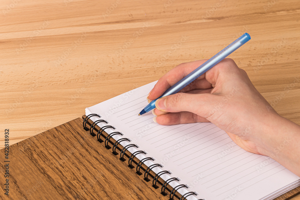 A man writes with a pen in an open notepad with white pages and a wooden brown box-spring cover that lies on the table A man writes with a pen in an open notepad with white pages and a wooden brown box-spring cover that lies on the table