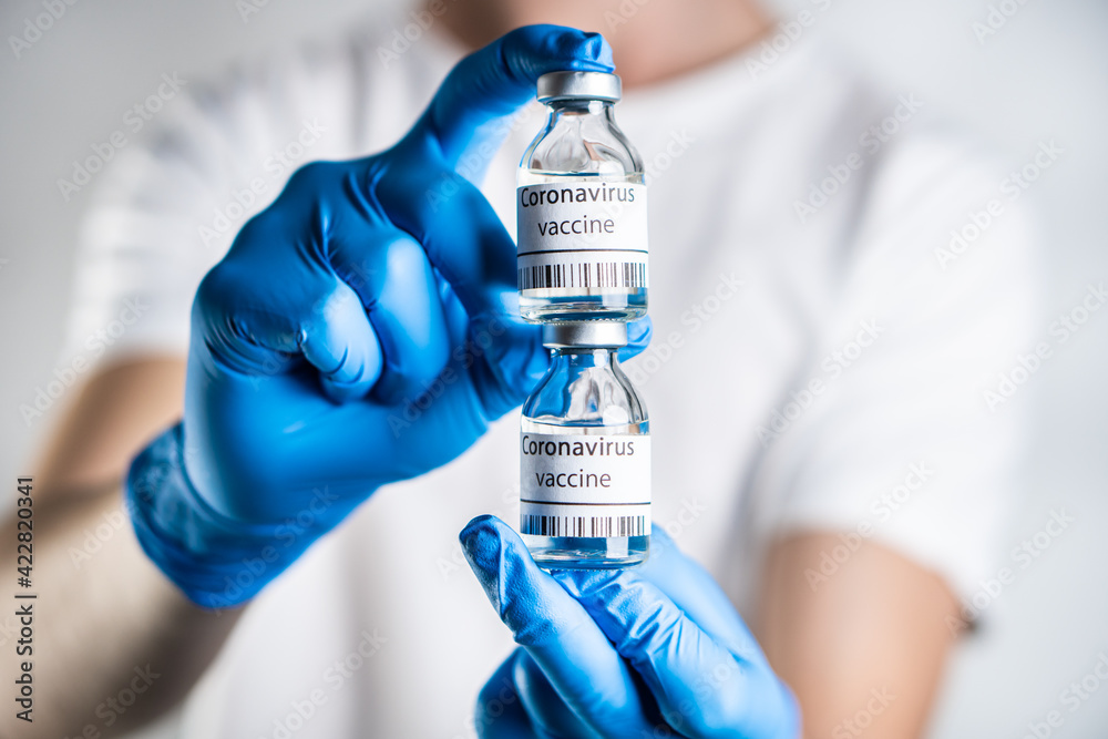 The doctor holds two coronavirus vaccines in his hand. He has blue rubber gloves on his hands, which serve as protection against coronavirus infection. The doctor holds two coronavirus vaccines in his hand. He has blue rubber gloves on his hands, which serve as protection against coronavirus infection.