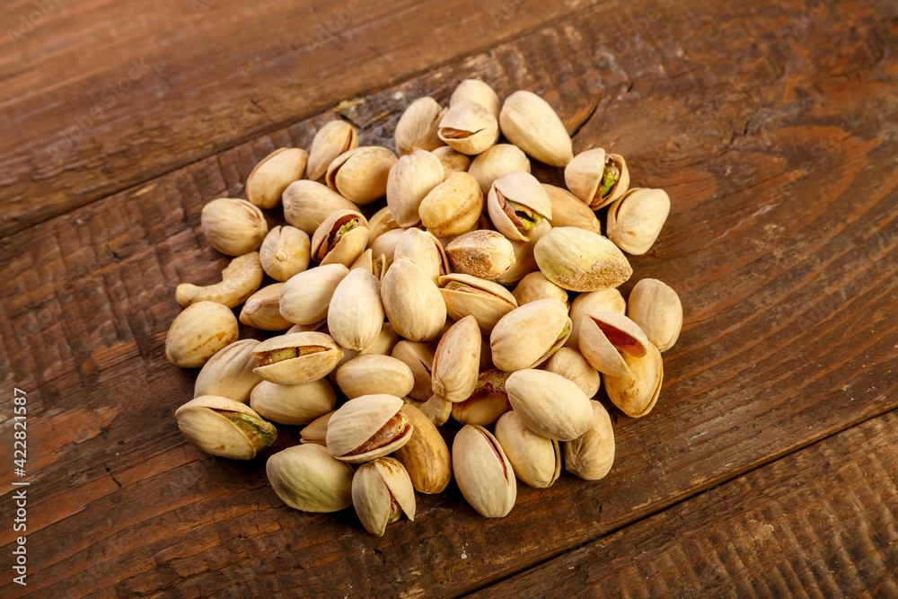 Pistachio nuts are sprinkled on a dark wooden table. Pistachio nuts are sprinkled on a dark wooden table.