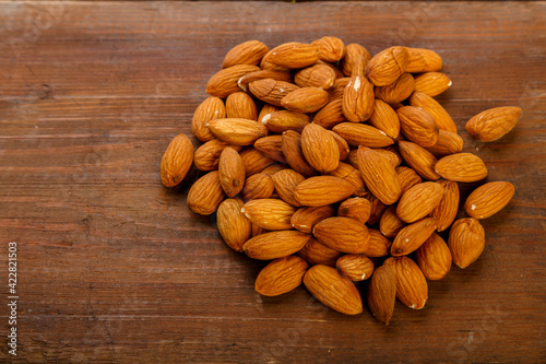 Almond nuts are sprinkled on a dark wooden table.