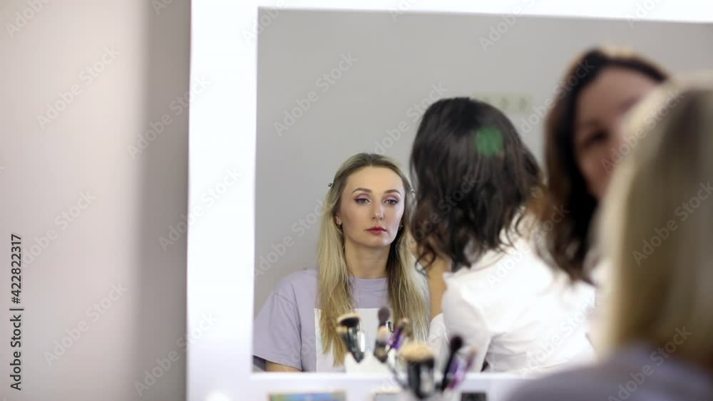 Brunette master in white shirt making make up for a blond model. View in a mirror. Brunette master in white shirt making make up for a blond model. View in a mirror.