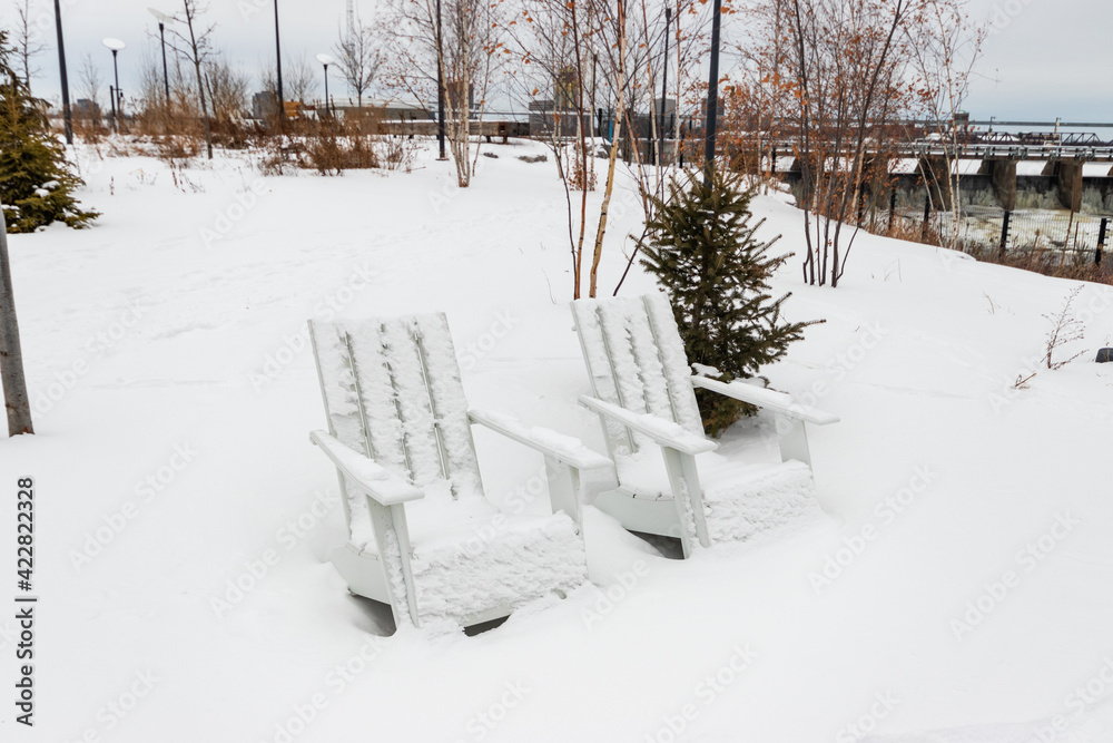 White wooden lawn chairs covered in snow, overlooking icy rapids from the Chaudière Falls (aka Akikodjiwan) in Ottawa, Canada