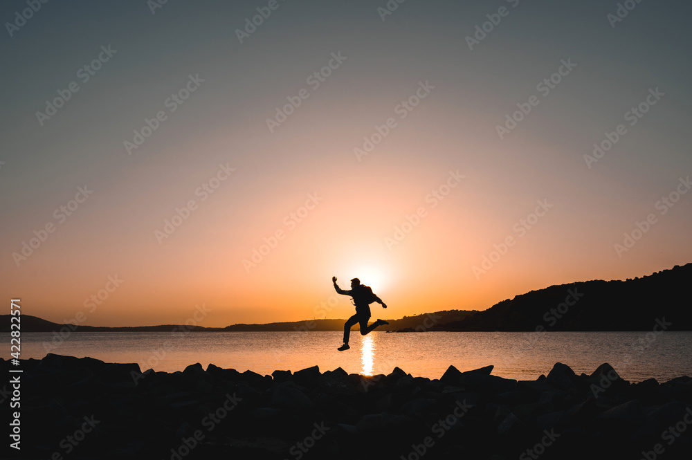 Silhouette of traveler on seashore jumping at the beach during sunset.