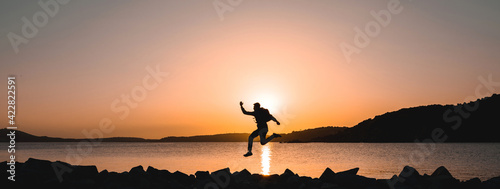 Horizontal banner silhouette of traveler on seashore jumping at the beach during sunset.