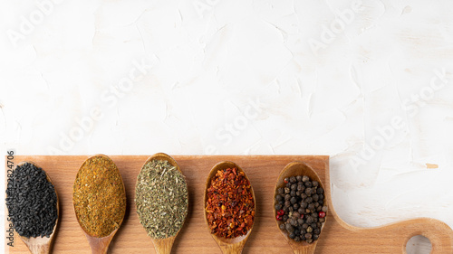 Collection of five spices on wooden spoons on wooden board on white cement background