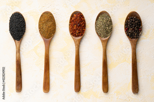 Collection of five spices on wooden spoons on yellow cement background