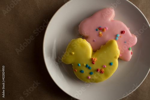 Traditional holiday Easter sugar cookies frosted in spring colors on a plate. Cookies are in rabbit and duck shapes with yellow duck in the foreground. © Xhico