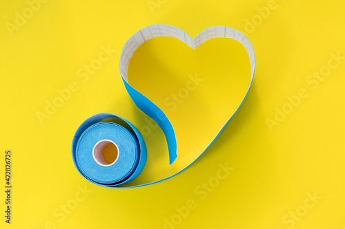A blue kinesio tape to support the muscles of the face and body lies on a yellow background. A heart-shaped tape. Sports medicine and rehabilitation. photo
