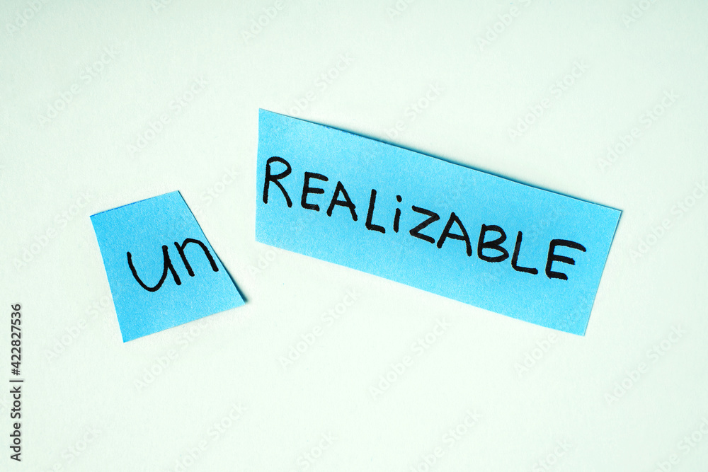 Scissors cutting paper with word UNREALIZABLE on blue background. Concept Scissors cutting paper with word UNREALIZABLE on blue background. Concept