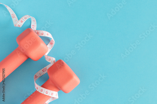 Dumbbells and measuring tape on blue background. Fitness, sport, workout flatlay