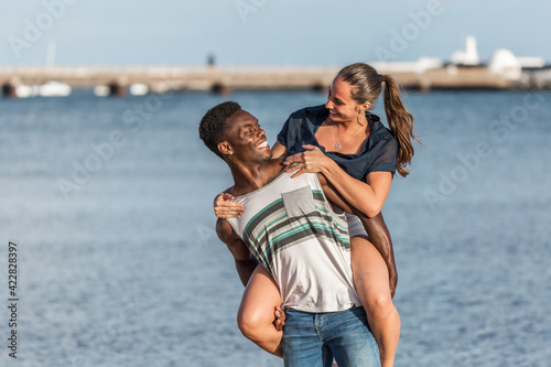 Black man giving piggyback ride to woman near sea