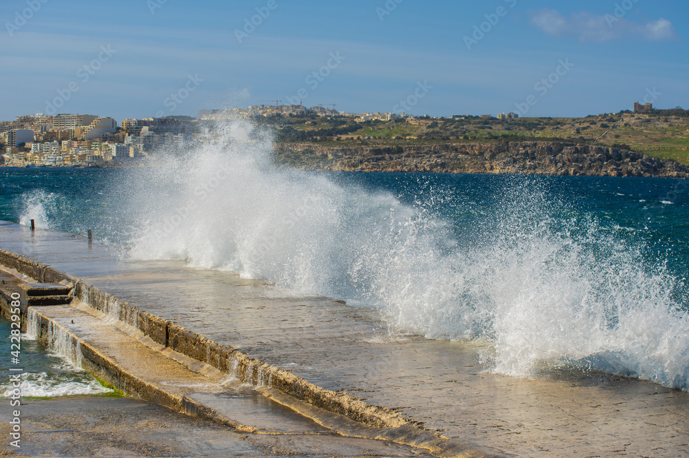 Waves crashing over a pier. Stormy beautiful blue mediterranean sea, city at background. Picture taken from Islet Promenade. Selective focus.