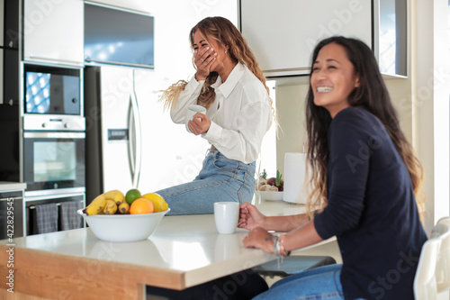 Two friends having coffee together in the kitchen at home - Sisters spending time together in the morning before going to work