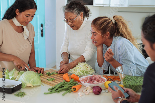 Filipino family cooking together at home - Granddaughters helping their grandmother to cook a traditional asian meal - Senior woman teaching a recipe to her daughter and granddaughters