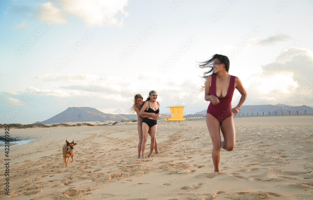 Grandmother and granddaughters having fun at the beach together - Filipino family enjoy the day at the sea with their dog - Senior woman and two young women wearing bikini