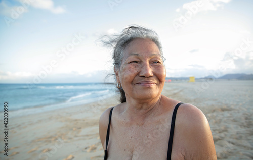 Beautiful senior woman standing at the beach, wearing a black bikini - Filipino mature woman smiling and enjoying her time on vacation