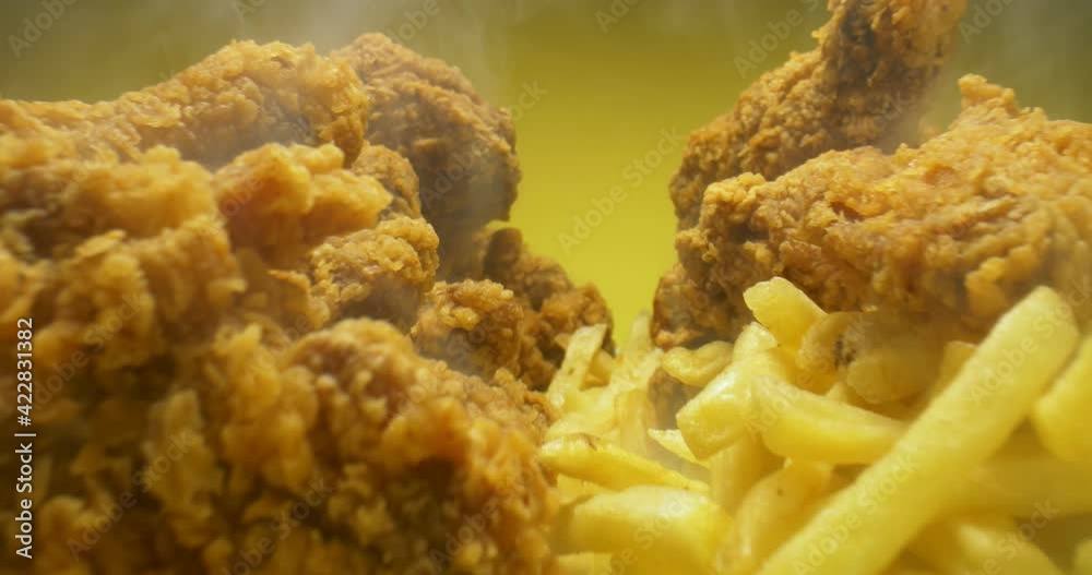 detailed extreme close-up of French fries and crispy chicken wings on a plate with smoke on yellow background.