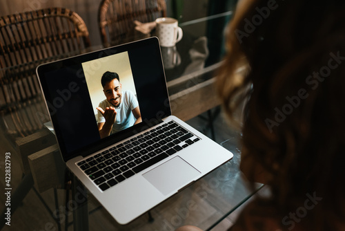 Rear view of a man in a video call conversation with an attractive woman giving a kiss. Man enjoying a nice long distance conversation using a laptop application. Online communication photo